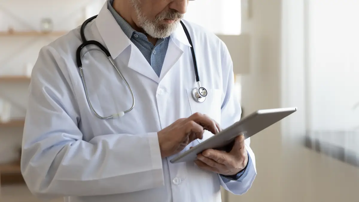 Doctor in a white coat with a stethoscope reading on a tablet