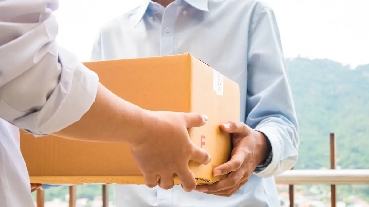 Hands passing a cardboard parcel to a customer at their home