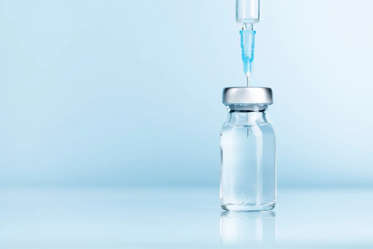 Glass medicine vial with a syringe needle drawing from it